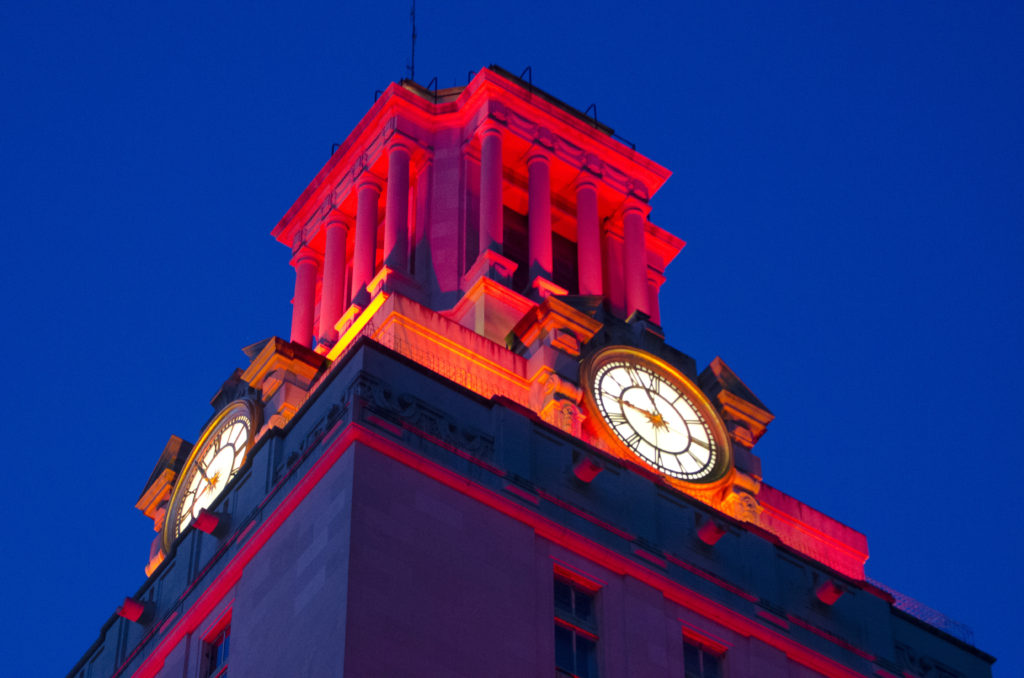 Top of the UT Tower glows orange against a dark blue background