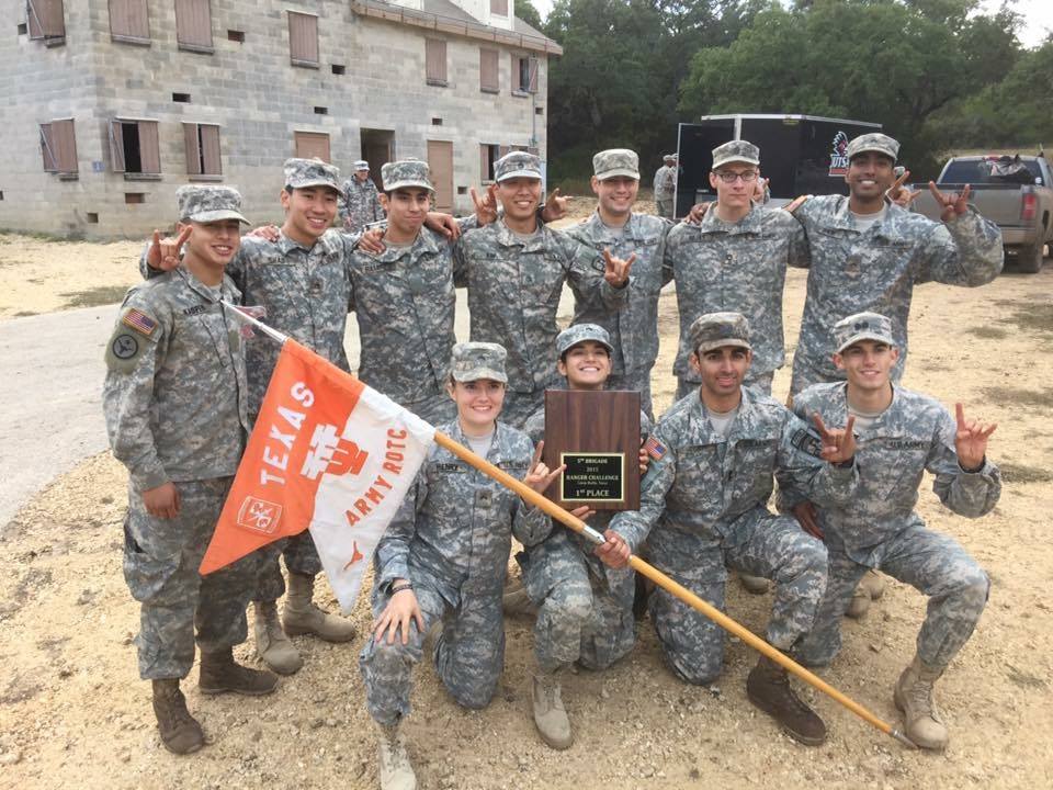 ROTC Students pose in uniform with a UT Texas Army ROTC Flag and plaque while showing the UT Hookem sign with their hands
