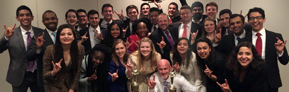 A group of Texas Speech students pictured with two trophies and each showing the hookem sign