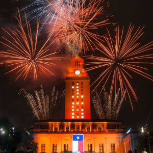 The UT Tower shines with burnt orange lights and the number “16” displayed on its sides and fireworks in the background.