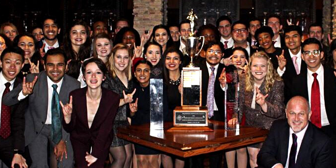 The UT Speech team shown displaying the hookem sign around a large trophy
