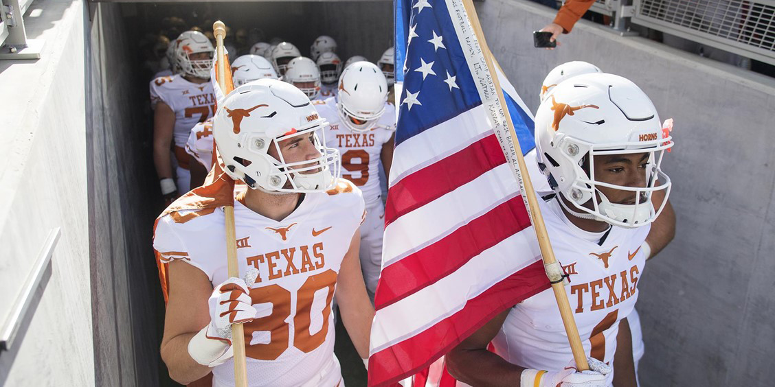 UT football team walking out with US flag. 
