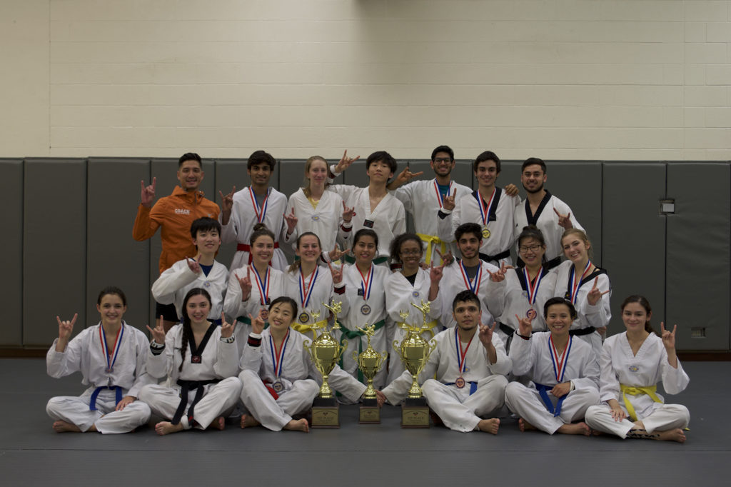 TaeKwonDo students pose with three trophies. Each student is showing the hookem sign with their hand
