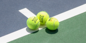 Three Big 12 branded tennis balls on tennis court