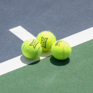 Three Big 12 branded tennis balls on tennis court