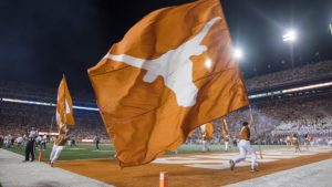 Texas cheerleaders run on football field carrying giant, burnt orange Longhorn flag