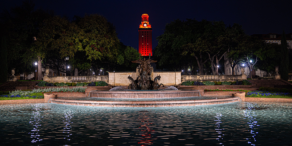 The UT Tower shines with burnt orange lights as seen from Littlefield Fountain