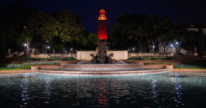 The UT Tower shines with burnt orange lights at night with Littlefield Fountain in the foreground