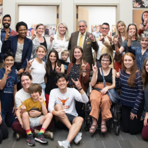 A group of people poses for a picture while showing their Hook Em Horns hand signs.