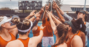 Members of the Women's Tennis Team huddle together in a circle and hold up their "Hook Em Horns" hand sign in the middle