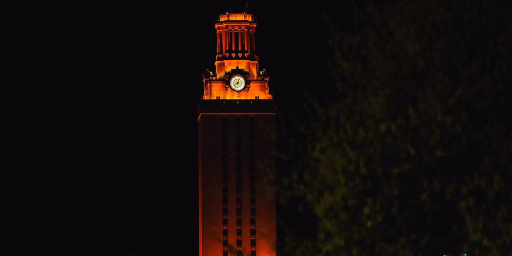 The UT Tower shines with burnt orange lights in front of a dark night sky.