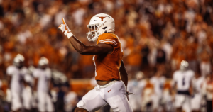 A Texas Football player runs down the field and points his finger in the air in celebration.