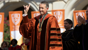President Jay Hartzell wears academic regalia and poses for a picture with his “Hook Em Horns” hand sign up.
