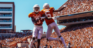 Two Texas Football players leap in the air in celebration.