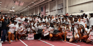 Members of the Texas track and field teams pose for a celebratory picture while holding trophies, waving signs and wearing clothes that all show they won the Big 12 Championships.