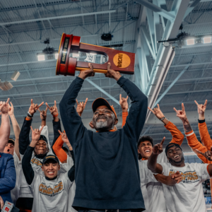 Members of the Texas Track and Field team celebrate as their coach holds up the national championship trophy over his head.