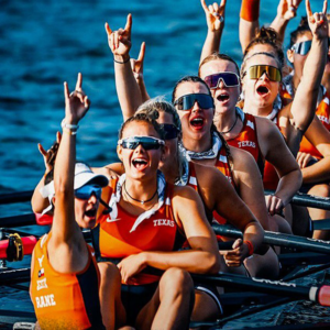 Members of Texas Rowing hold up their hook em horns hand sign while in their boat on the water.